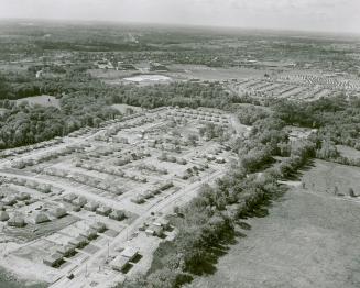 Foreground shows aerial view of housing development with uniformly spaced homes on flat, treele ...
