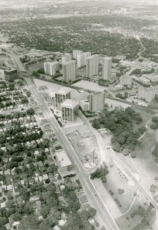 Aerial view of several clusters of tall buildings right of multi-lane roadway; overhead view of ...
