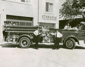 Men in dark, peaked service caps, white shirts, dark pants and ties- pose with fire truck in fr ...