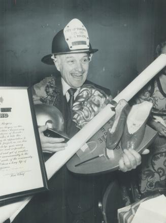 Harry Rogers, city property commissioner, wears a fire chief's helmet and carries other gifts presented to him by city employees at a gala to mark his(...)