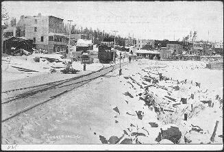 Black and white photograph of train tracks leading into a small bush town.
