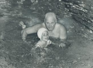 A swimming certificate for every public school graduate should be compulsory, says famous swimming coach Gus Ryder shown here teaching 4-year old Kim Chapman to swim the breast stroke