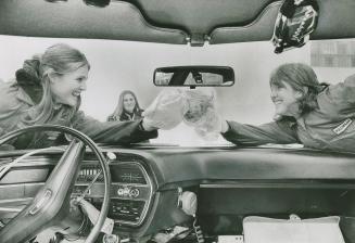 Driver's seat view from car interior of steering wheel, dashboard, and two girls reaching acros ...