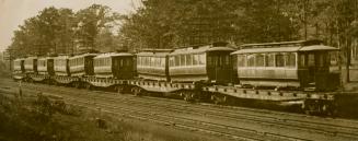 Black and white photograph of street cards being transported by railroad.