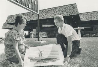 Tribute to hard work, the Bak family's architect- designed roadside open-air market, is in the background as Casey Bak and his wife Freda look at the architect's drawings on how it will appear when the windmill is completed as a landmark in the Holland area. The market was planned by Casey's father, Walter, who died in January at age of 74.