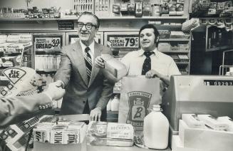 Still lean and tought at 74, Frank Bazos (left), chairman of Beeker Milk Co. Ltd., helps manager Andrew Karastamatis to serve customer in store on Toronto's Bedford Rd. Becker chain, biggest convenience-style grocer in Ontario, opened 500th store this week.