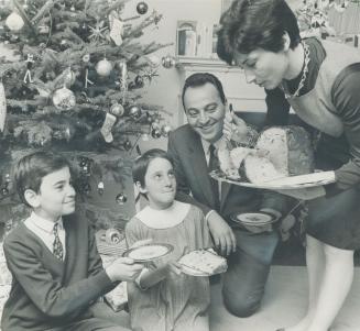 An Italian custom at Chritmas is the eating of a traditional cade-bread called panettone, which many Italian-Canadian families will partake of on Christmas Day. Enjoying it her are Italian Trade Commissioner Mario Castagna, his wife, and children Palo, 10, and Diana, 7, before their Christmas tree.