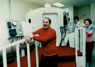 Tank: Dr. Richard Cole is standing in front of the Oakville Hyperbaric Centre's oxygen chamber. The clinic provides treatment for 104 multiple sclerosis sufferers, 70 per cent of whom have experienced improvements. At right is centre coordinator Judy macNeill and Cole's wife.