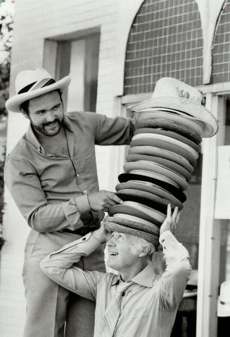 Mad hatter? George Catleugh tries to balance 25 hats on his head with help from his son Keith. The Catleughs sell, make and clean hats in their shop on Avenue Rd. Hats are making a comeback, they say.