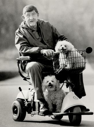 Along for the ride: Editor Max Crittenden, who suffers from multiple sclerosis, rides through the park on his electrically powered wheelchair scooter with his two poodles. Crittenden had formerly relied on a manual push chair, but fatigue made it difficult for him to go far in it.