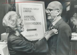 Before entering annual meeting of Traders Group, company chairman Henry Dynes gets a carnation for his lapel from employee Dorothy Tustin. Dynes received prolonged applause from shareholders when he said: Be we Liberal, Conservative or NDP, we and our elected representatives must endorse one position - that of a united Canada. He advocated non-partisan committee to work toward unity.
