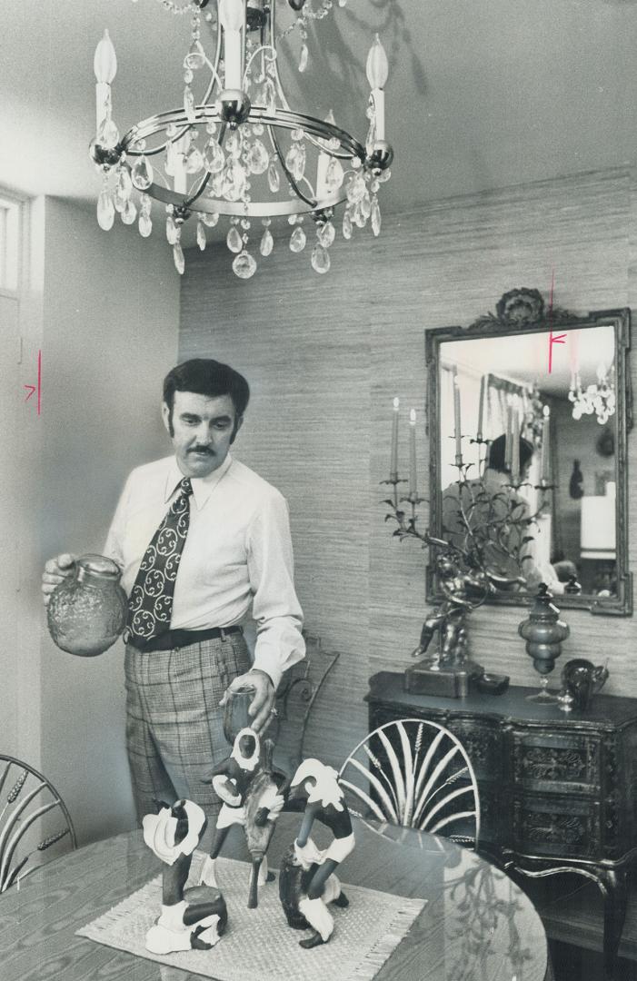 Display designer Clive Deverath pours a cool drink in his downtown Toronto high rise. His apartment mixes moods, periods, as seen in these pottery figures of African musicians in foreground and Italian decor in background.
