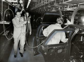 Grass roots management: General Motors Corp. president E. M. (Pete) Estes holds paint hose on production line of new GM paint plant dedicated yesterday.