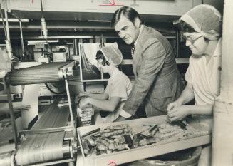 Donald H. Lovell, nely-elected president of the Confectionery Manufacturers Association of Canada, is seen on a visit to packaging assembly line at the candy plant of William Neilson Ltd. on Gladstone Ave. Busy packing Danish bars are Antoinette Cauchi (left) and Gwen Strickland. Lovell, 47, is vice-president of marketing and Candy King - especially of his west-end home neighborhood - and unofficially of Canada.