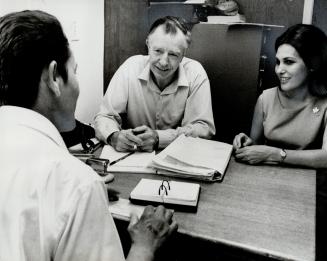 Help for a new Canadian: A Portuguese immigrant, with back to camera, is interviewed by Milton Little, co-ordinator of the Ontario Human Rights Commission's Services for Working People, and his Portuguese interpreter, Emilia Lopes