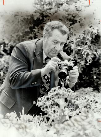 Special close-up lens on his camera is used by 66-year-old Ted Maginn as he photographs a fuschia bud at the Centennial Park greenhouse