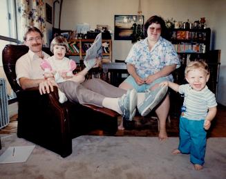 Average family: Alan Marshall, left, holds daughter Katie, 3 1/2, as he and wife Betty, and son, 13-month-old Daniel watch details on Finance Michael Wilson's tax reforms on TV