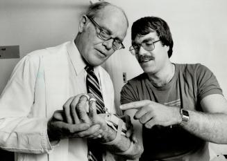 Treating the trauma: Dr. James Murray, head of Sunnybrook Medical Centre's hand unit straps a finger manipluator onto the palm of 23-year-old John Boothby of Orilla. Boothby's right hand was smashed in an car accident in June, 1982. There were 23 different pieces of bone. Says Murray: . . . the hand is such an important part of the body, not just physically but aesthetically.
