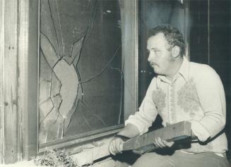 Armed with a club, John Semple of Burlington sits next to a window in his home smashed in one of a series of attacks on the house by what police suspect is a loosely organized bunch of hooligans