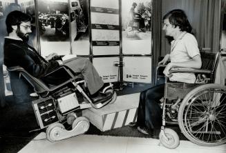 Curb climber: Tim Skene, representing the Quebec firm that developed the new wheelchair with a grant from Transport Canada, shows off its curb-climbing ability to Jim Gerrond, a cerebral palsy victim, at the first international Conference on Rehabilitation Engineering at the Sheraton Centre