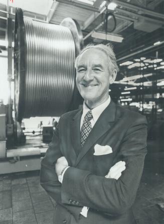 Top business spokesman J. Hugh Stevens stands in front of mammoth wire spool at Laird Dr. plant of Canada Wire and Cable Co. Ltd., of which he's chief executive. Stevens, who today became persident of the Canadian Manufactures Association says companies must become more competitive to create more jobs.