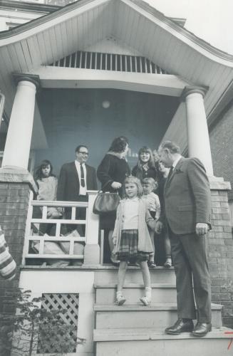 Delighted with their new home, found for them by Alderman Mike Grayson (right foreground), John Taylor (right background), his wife Myrtle, and their six children stand on porch of six-bedroom house in Toronto's west end