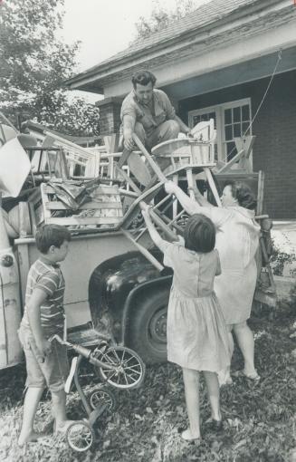 Moving into new home they had despaired of finding for their family of eight children, Albert Treadwell hands furniture down from top of truck to his wife Velma and daughter Vivian, 10, while son Gordon, 9, takes his tricycle