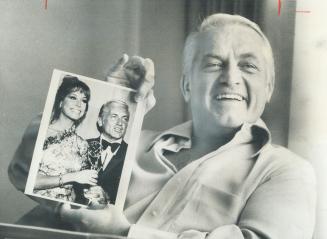 Actor Ted Knight, in Toronto for luncheon address, holds photo of him and Mary Tyler Moore, in whose show he portrays bumbling telecaster