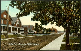 Shows a quiet, unpaved residential street with wide verges and paved sidewalks.