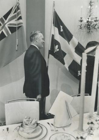 Quebec's Jean Lesage stands between two flags. Park Plaza hotel reception last night was in honor of visiting premier.