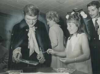 Liberace signs autographs for Marie Sturman, 11, and Fred Riley, 31, in his dressing room at the O'Keefe Centre