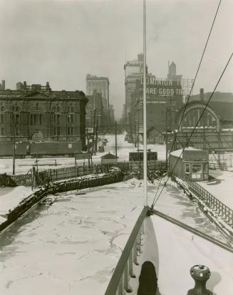 Image shows some Harbor buildings with streets and lake covered with snow.