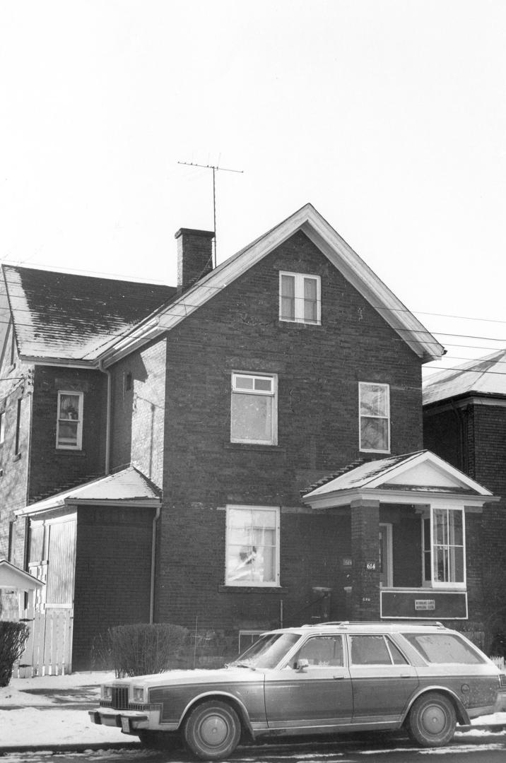 Shows a three-storey brick house with a porch, a TV antenna and a 1970s-era station wagon. Take…