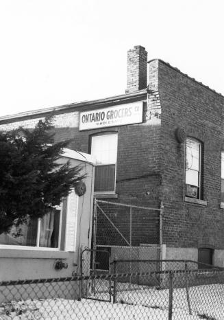 A corner view, taken in winter, of a blocky brick building. There is a half-storey façade, with…