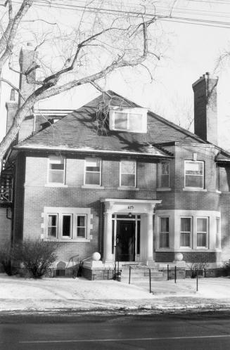 Front view of a large square brick house with a portico over the entry, and decorative stonewor ...