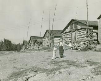 Child standing next to log cabins in McIntyre, Ont.