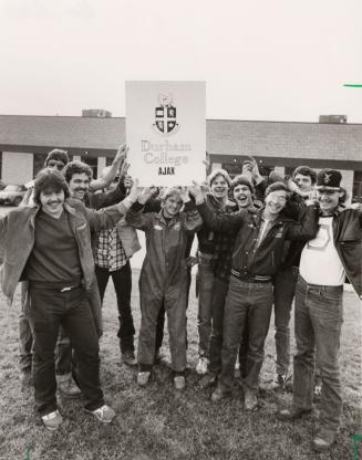 Students holding up Durham College crest in front of Durham College. Ajax, Ontario