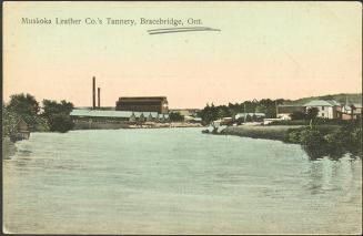 Colorized photograph of industrial buildings beside a body of water.