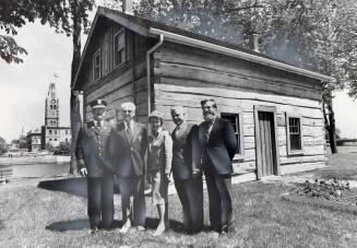 Fire Chief Fred Hosking, Bud [illegible], ex-mayor Robin Jeffrey, historian Nick Mika, and centennial executive director Tom Baird outside the log cabin that was their centennial headquarters. Belleville, Ontario