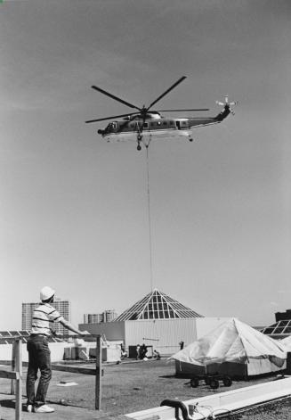 Helicopter unloads air handling units being installed on the roof of the Bramalea City Centre. Bramalea, Ontario