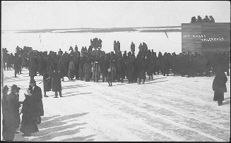 Photograph shows a crowd of people standing on a frozen lake.