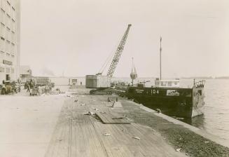 Image shows a Harbour view with a crane on it and a barge on the water.