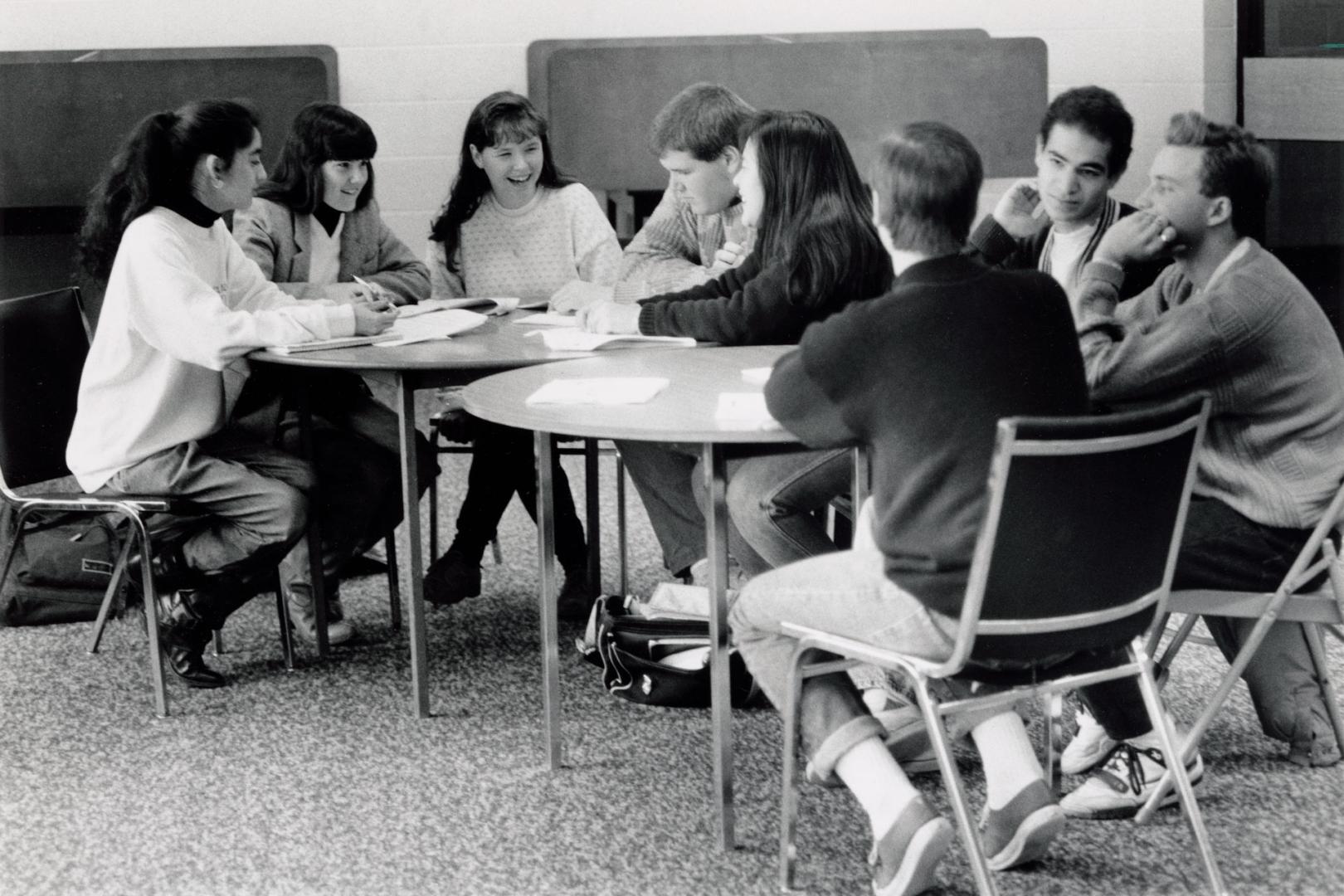 Eight high school students in chairs around two round tables, laughing.