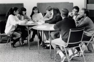 Eight high school students in chairs around two round tables, laughing.
