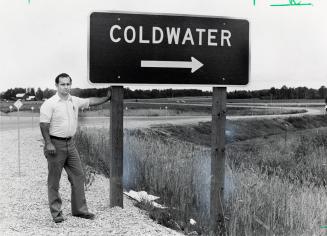 Businessman Ken Athron beside Coldwater sign on Highway 400. Coldwater, Ontario