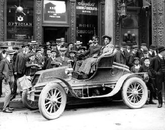 Man and woman in ''Beattie'' automobile in front of stores in the King Edward Hotel, 43 King Street East