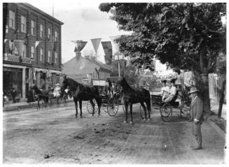 A photo of two horses, drawing two four-wheeled carriages on the main street of Picton. In the  ...