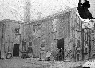 Image shows a few people standing beside open doors of brickmakers' supplies building.