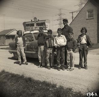 Popcorn vendor l. Nicholson posing with children on Greenview Avenue near Hendon Avenue, North York, Ontario