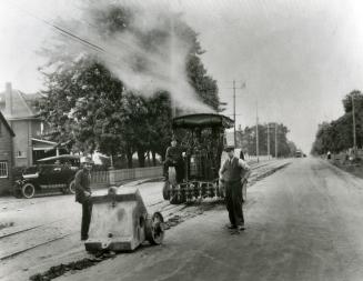 Workers pose in front of steaming road re-surfacing equipment in the 1920s.